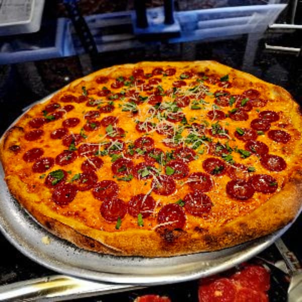 A large, round pepperoni pizza from Hartsdale House of Pizza, topped with cheese and herbs.