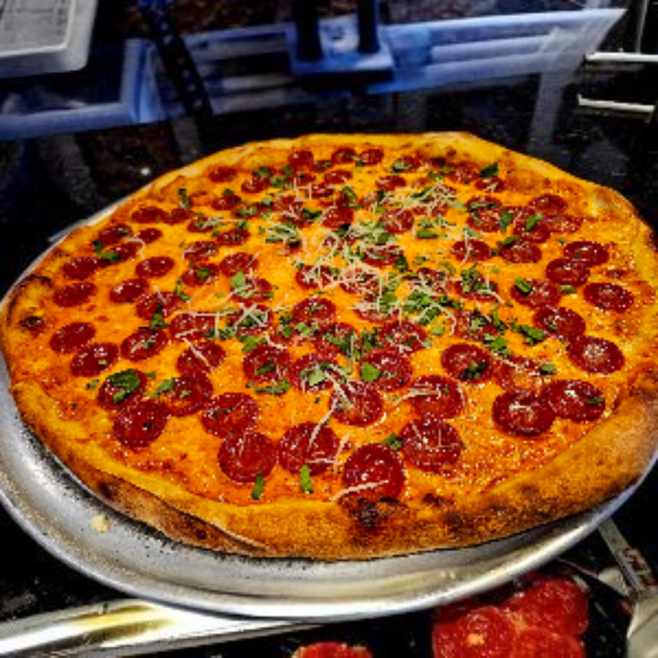 A large, round pepperoni pizza from Hartsdale House of Pizza, topped with cheese and herbs.