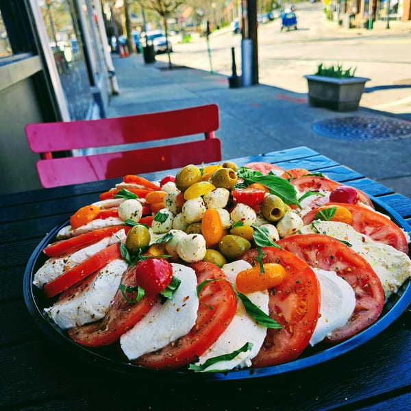 Caprese salad with sliced tomatoes, mozzarella, basil, olives, and cherry tomatoes on a black platter.