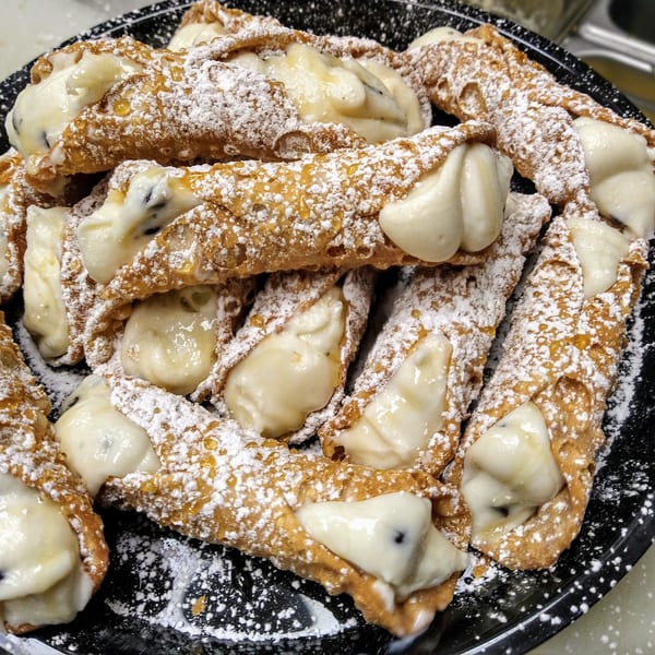 A platter of cannolis, filled with cream and sprinkled with powdered sugar and honey.