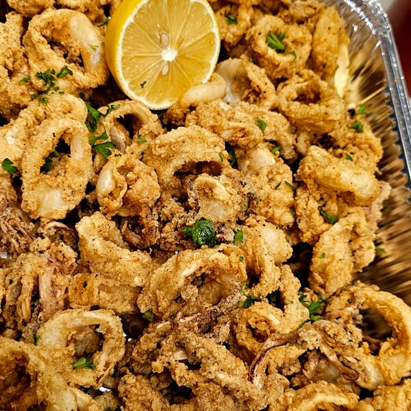 Crispy fried calamari rings with parsley and a lemon wedge in a foil tray.