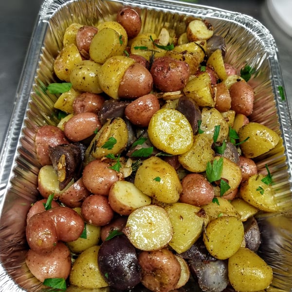 Roasted red, yellow, and purple potatoes with herbs and spices in a foil pan.