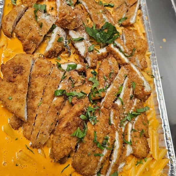 Crispy breaded chicken cutlets over penne pasta in a creamy orange sauce, garnished with fresh basil.