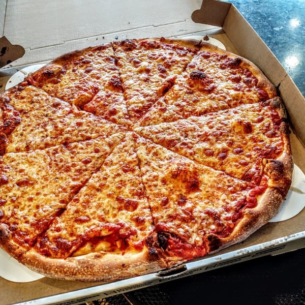 A large, freshly baked cheese pizza, sliced into eight pieces, in a cardboard delivery box.