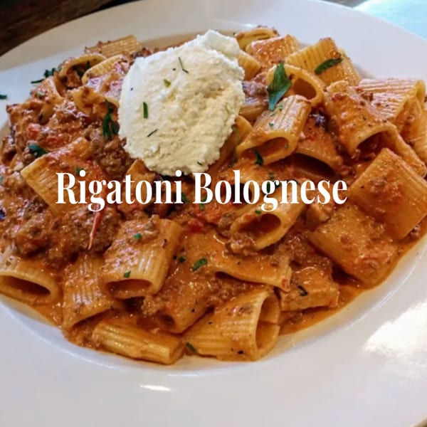 Rigatoni Bolognese pasta with meat sauce and a dollop of ricotta cheese on a white plate.