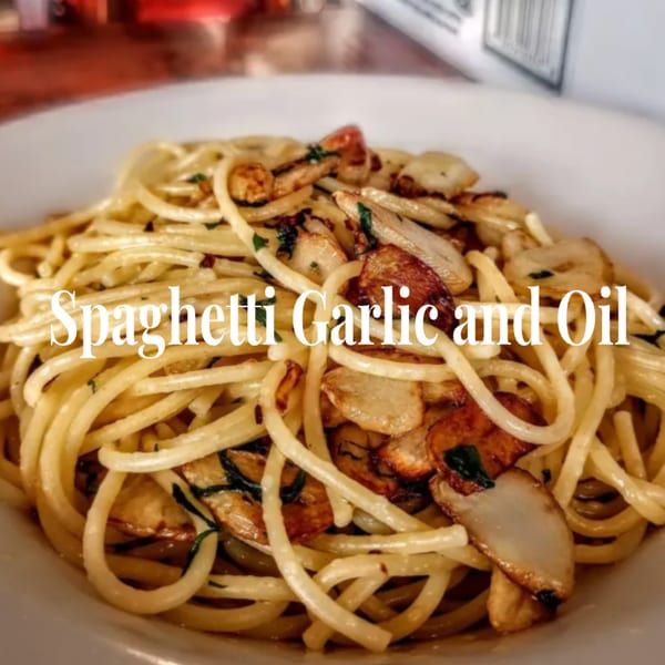 A close-up of spaghetti aglio e olio with toasted garlic slices and herbs in a white bowl.