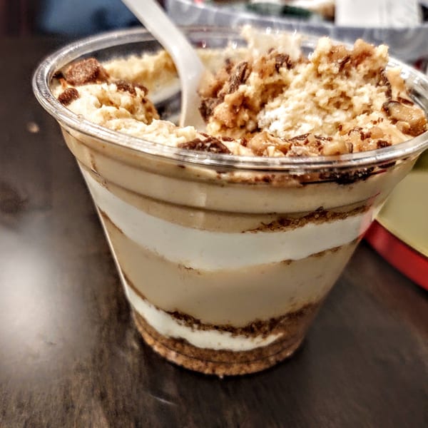 Layered dessert cup with cream, crumbs, and a spoon, on a dark table at Hartsdale House of Pizza.