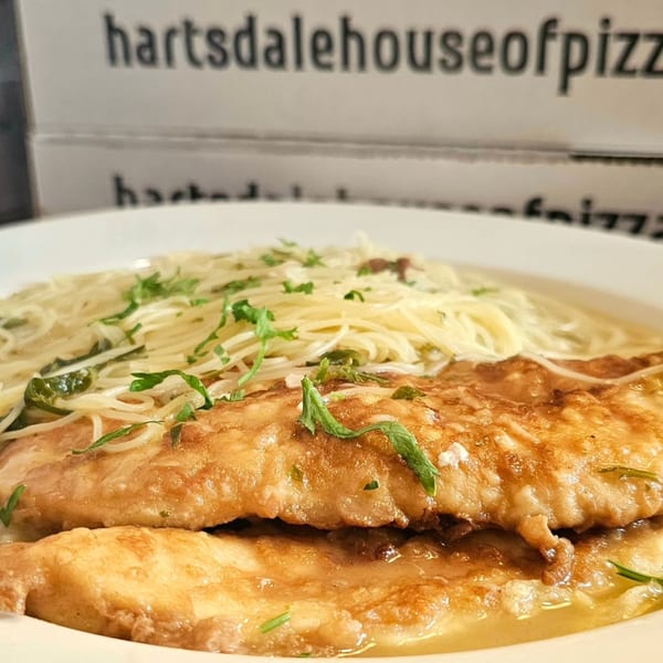 Chicken Francese with angel hair pasta and fresh herbs, with pizza boxes in the background.