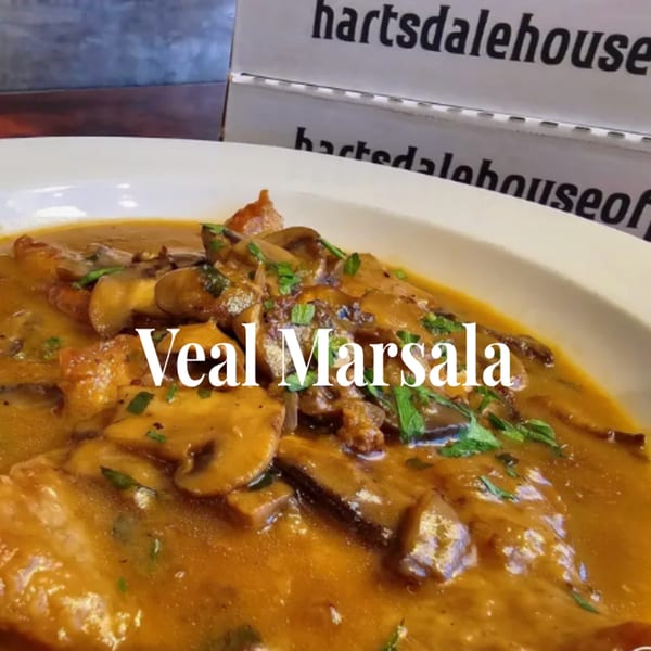 Veal Marsala with mushrooms and parsley in a rich brown sauce, with pizza boxes in the background.