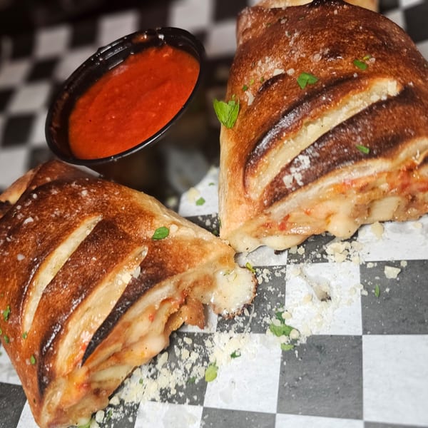 Two golden-brown calzones with melted cheese and a side of red marinara sauce on a checkered surface.