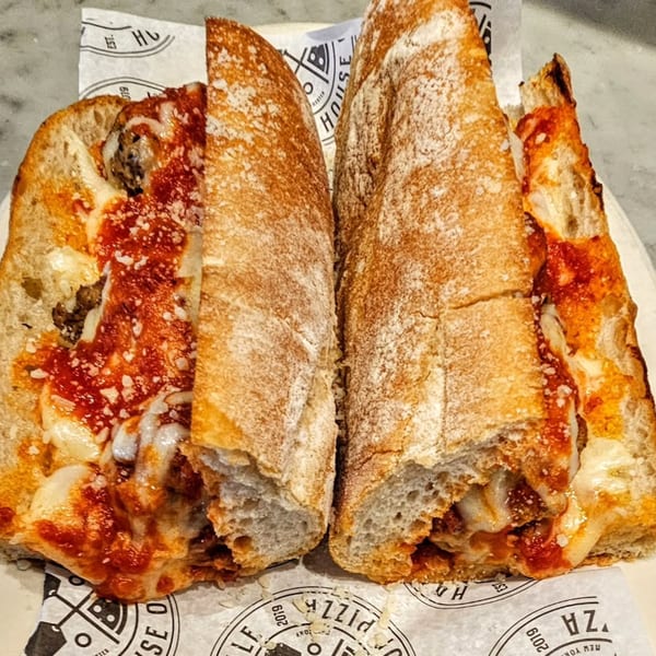A meatball hero sandwich, cut in half, with melted cheese, marinara sauce, and parmesan.
