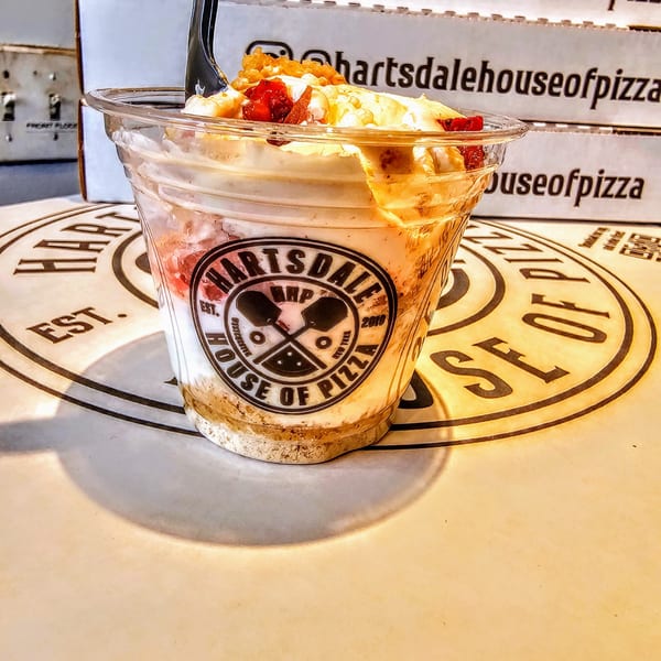 A clear cup of dessert with a Hartsdale House of Pizza logo, on a pizza box.