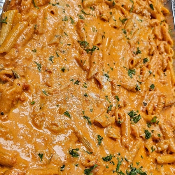 Close-up of penne pasta in creamy orange sauce, garnished with parsley and parmesan cheese.