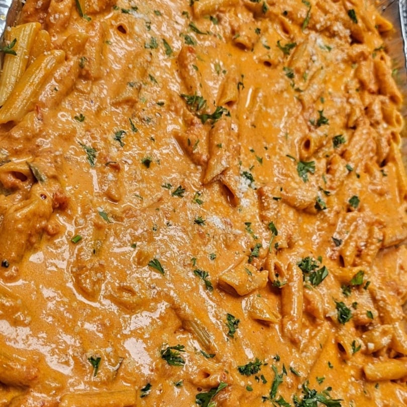 Close-up of penne pasta in creamy orange sauce, garnished with parsley and parmesan cheese.