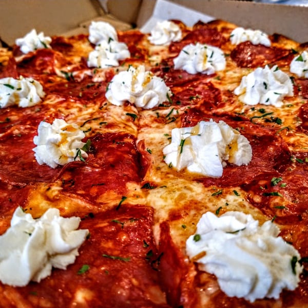 Close-up of a pepperoni pizza from Hartsdale House of Pizza, topped with dollops of ricotta cheese and herbs.