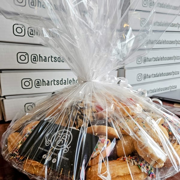 A cellophane-wrapped cookie platter with a business card, in front of stacked Hartsdale House of Pizza boxes.