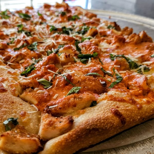 Close-up of a Buffalo chicken pizza from Hartsdale House of Pizza, topped with cheese and basil.