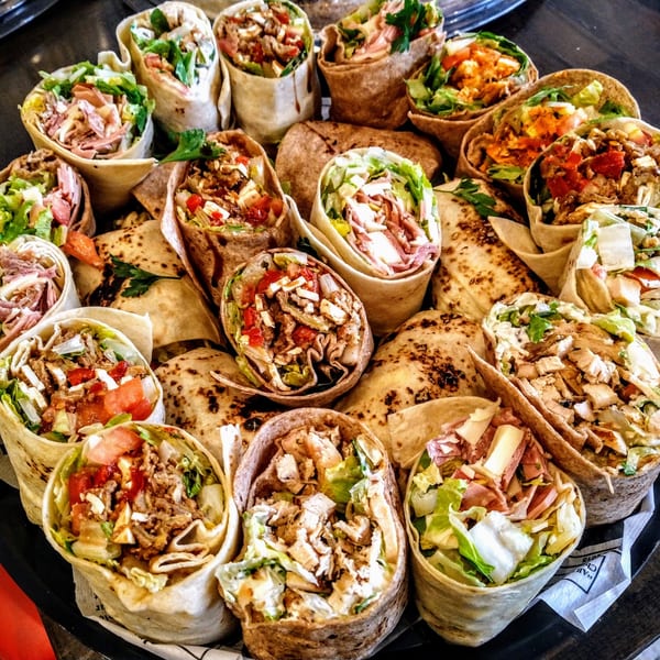 A platter of various wraps, including chicken, ham, and beef, with fresh vegetables and cheese.