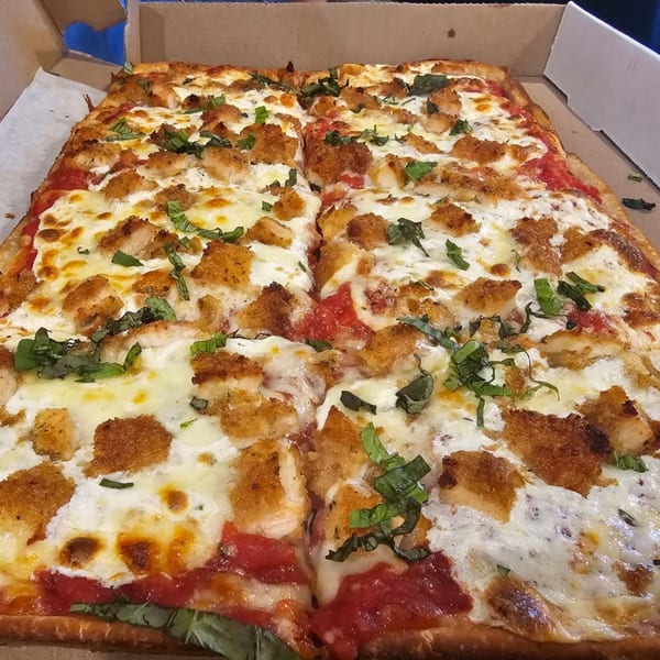 A rectangular Hartsdale House of Pizza chicken parmesan pizza, topped with fresh basil, in a cardboard box.